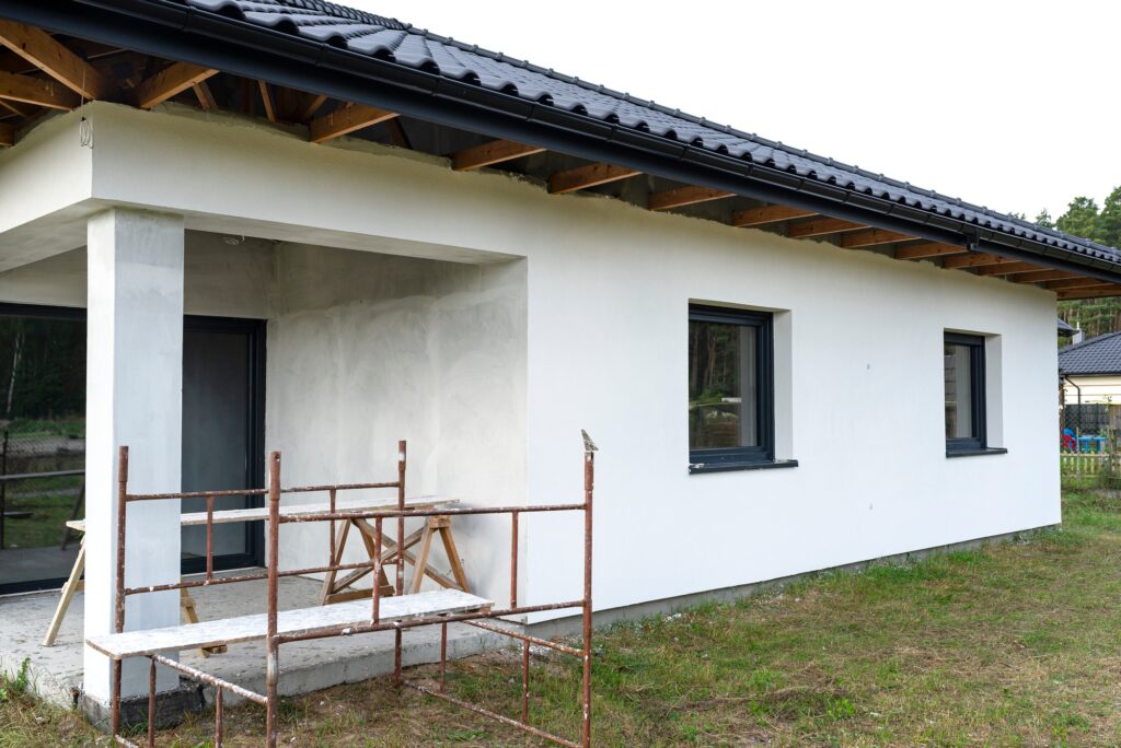 A newly applied layer of white silicone plaster on the wall of the house, visible metal scaffolding